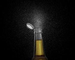 foto de primer plano de una botella de cerveza marrón salpicando gotas de cerveza sobre un fondo negro. gorra de cerveza volando encima de la botella. renderizado 3d