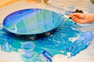 The process of creating a home-made trendy abstract modern pattern painted with a brush of acrylic blue multi-colored resin on a round wooden board photo