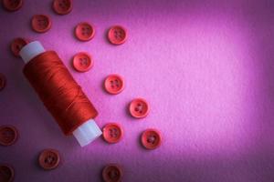 Beautiful texture with many round pink buttons for sewing, needlework and a coil of thread. Copy space. Flat lay. Pink, purple background photo