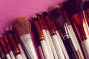 A set of beautiful different soft brushes for make-up from natural nap for beauty targeting and applying a tonal foundation in a stand and copy space on a pink, purple background photo