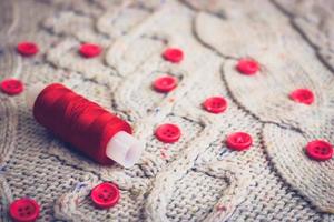 hermosa textura de un suéter natural cálido y suave, telas con un patrón de punto de hilo y pequeños botones redondos rojos para coser y una madeja de hilo rojo. el fondo foto