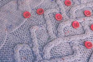 Beautiful texture of a soft warm natural sweater with a knitted pattern of yarn and red small round buttons for sewing. The background photo