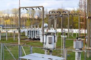 Large industrial iron metal transformer substation with transformers and high-voltage electrical equipment and wires with surge arresters to supply the city with electricity photo