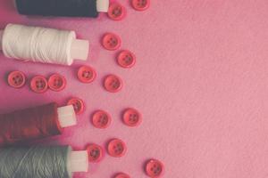 Beautiful texture with lots of round red buttons for sewing, needlework and skeins of spools of thread. Copy space. Flat lay. Pink, purple background photo