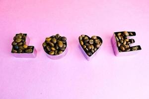 Beautiful texture with the word love for valentine's day inscription made from roasted selected brown natural aromatic Arabica coffee beans, robusta Copy space, flat lay, pink purple background photo