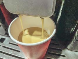 taza de café de cartón rojo en la que se vierte un delicioso café americano negro caliente vigorizante de la máquina de café en la oficina por la mañana foto
