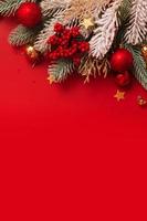 Christmas decoration and pine tree on red background with copy space. New Year greeting card. Flat lay. Vertical format photo