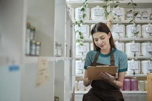 la tendera blanca revisa el stock de productos orgánicos naturales en la exhibición minorista en la tienda de recarga, tienda de comestibles sin residuos y sin plástico, estilos de vida ecológicos y sostenibles, contenedores reutilizables. foto