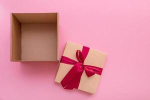 abra una caja de regalo vacía con una tapa con un lazo satinado junto a ella sobre un fondo rosa con espacio para copiar foto