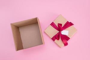 caja de regalo vacía abierta con lazo de cinta satinada y etiqueta vacía sobre fondo rosa foto