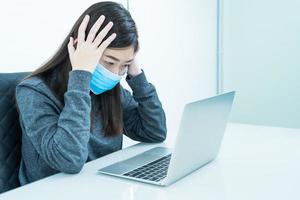 Woman using laptop on desk with headache wearing mask for protect Covid-19 photo