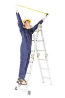 Handyman in uniform standing on ladder while using tape measure on white photo