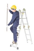 Handyman in uniform standing on ladder holding wood plank on white photo