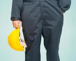 Worker standing in blue coverall holding yellow hardhat photo