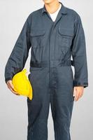 Worker standing in blue coverall holding hardhat photo