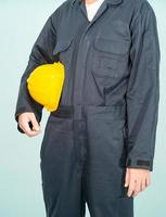 Worker standing in blue coverall holding yellow hardhat photo