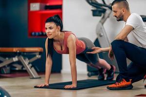 mujer haciendo ejercicios de tablones con entrenador en el gimnasio foto