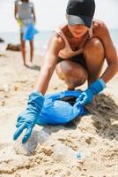 Volunteer Woman Collecting Litter In Garbage Bag On The Beach photo