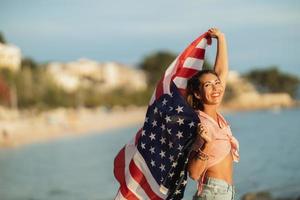 mujer con bandera nacional americana pasando el día en la playa foto