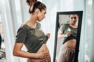 mujer tocando la barriga gorda mientras está de pie cerca del espejo foto