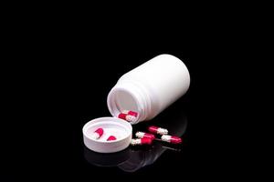 Medical pills flow from a white jar on an isolated black background with reflection photo