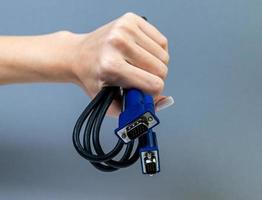 female hand holding VGA cable on gray background isolated photo