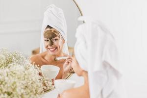Woman In Front Of Mirror Applying Facial Mask At The Beauty Salon photo