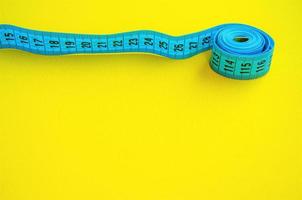 Sewing Measuring Tape on yellow background. Copy space for text. Bright blue measuring tape. photo