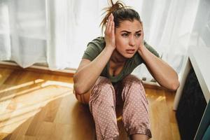 mujer que se siente ansiosa mientras está de pie cerca de la ventana en casa foto