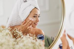 mujer frente al espejo aplicando crema hidratante en la cara en el salón de belleza foto