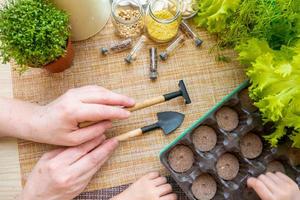 las macetas de turba, las herramientas y el suelo están listos para plantar semillas. cultivo de plántulas para jardinería. endecha plana con manos de bebé foto