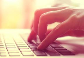 manos femeninas escribiendo en una laptop con luz de bengala foto