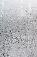 textura de una gota de lluvia sobre un fondo transparente húmedo de vidrio. tonificado en color gris foto