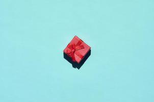 pequeña caja de regalo rosa roja se encuentra en el fondo de textura de papel de color azul pastel de moda en concepto mínimo foto