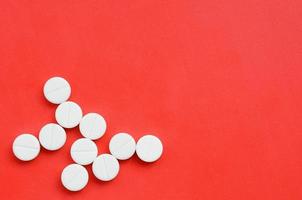 Several white tablets lie on a bright red background in the form of a bacterium. Background image on medicine and pharmaceutical topics photo
