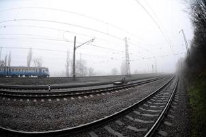 The Ukrainian suburban train rushes along the railway in a misty morning. Fisheye photo with increased distortion