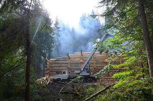 el proceso de construcción de una casa de madera a partir de vigas de madera de forma cilíndrica. grúa en condiciones de trabajo foto