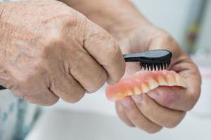 Asian senior or elderly old woman patient use toothbrush to clean partial denture of replacement teeth. photo