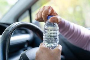 Asian woman driver holding bottle for drink water while driving a car. Plastic hot water bottle cause fire. photo