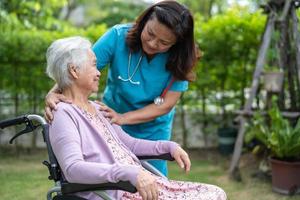Doctor caregiver help and care Asian senior or elderly old lady woman patient sitting on wheelchair in park at nursing hospital, healthy strong medical concept photo