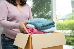 Holding clothing donation box with used clothes at home to support help for poor people in the world. photo