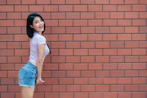 retrato de una chica hipster en el fondo de la pared de ladrillo, hermosa mujer asiática posa para tomar una foto