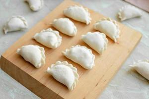 Beautiful raw stuffed dumplings on a wooden cutting board photo
