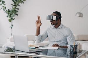 African american man architect in virtual reality glasses works on project in VR on laptop in office photo