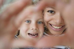 Adopted daughter, mom showing heart gesture together, symbol of love, care, support. Happy adoption photo