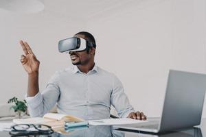 African american businessman in vr glasses working on business project in virtual reality at laptop photo