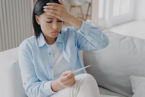 Unhealthy female holding thermometer, checking body temperature, suffers from flu or coronavirus photo