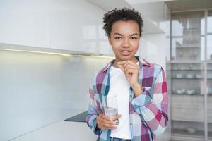 niña de raza mixta toma pastillas, vitaminas, suplemento dietético para el bienestar sosteniendo un vaso de agua