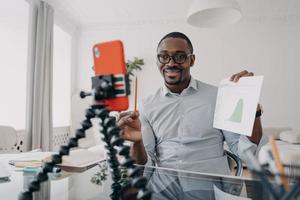 African american businessman shows economic statistics, consulting client by video call, using phone photo