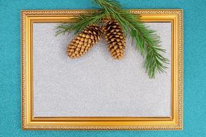 Golden frame with sparkling silver backdrop with spruce branch and cones on blue shiny background. Christmas, New Year. Copy space photo